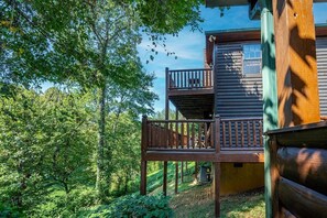 A wooden cabin with a balcony, surrounded by dense greenery.
