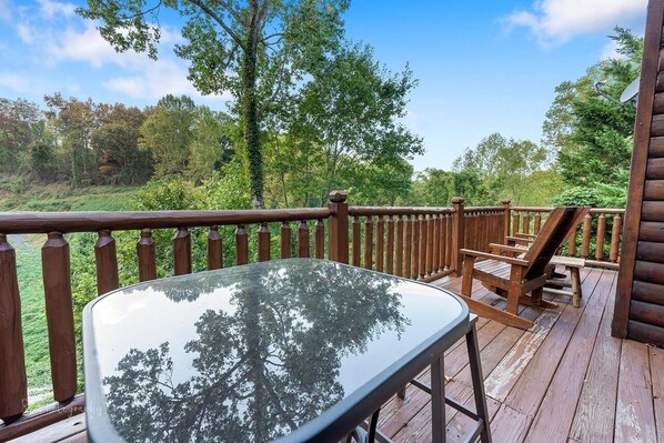 A wooden deck with a glass table and chairs, overlooking a forested area. - Paw Prints (Sevierville)