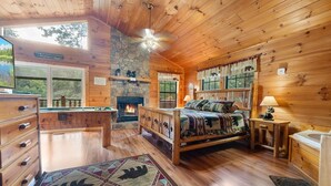A cozy cabin interior with a stone fireplace, wooden bed, and a pool table. - Paw Prints (Sevierville)
