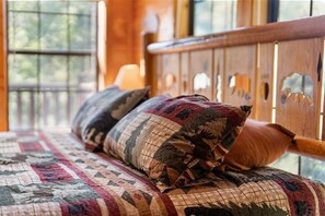 A bed with a quilted bedspread and two pillows, a wooden headboard with cut-out designs, and a window with a view of trees.