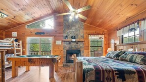 A cozy cabin with a pool table, a bed with a patterned quilt, a stone fireplace, and a ceiling fan. - Paw Prints (Sevierville)