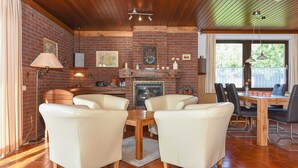 A cozy living room with brick walls, a fireplace, and a dining area with a wooden table and chairs. - Holiday house in Taddigshörn 303 - holiday houses beach castles (Esens)