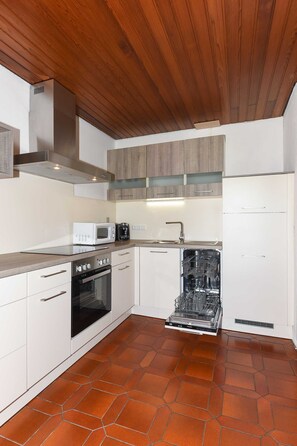 A modern kitchen with white cabinetry, a wooden ceiling, and a tiled floor.