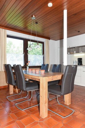 A dining area with a wooden table, black chairs, and a view of the outdoors through large windows.
