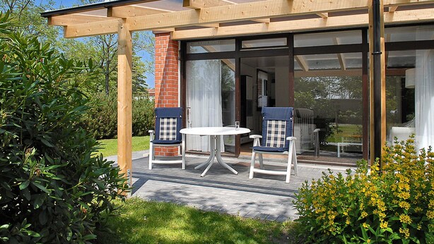 A modern outdoor patio with a glass enclosure, two chairs, and a table. - Holiday house in Taddigshörn 303 - holiday houses beach castles (Esens)
