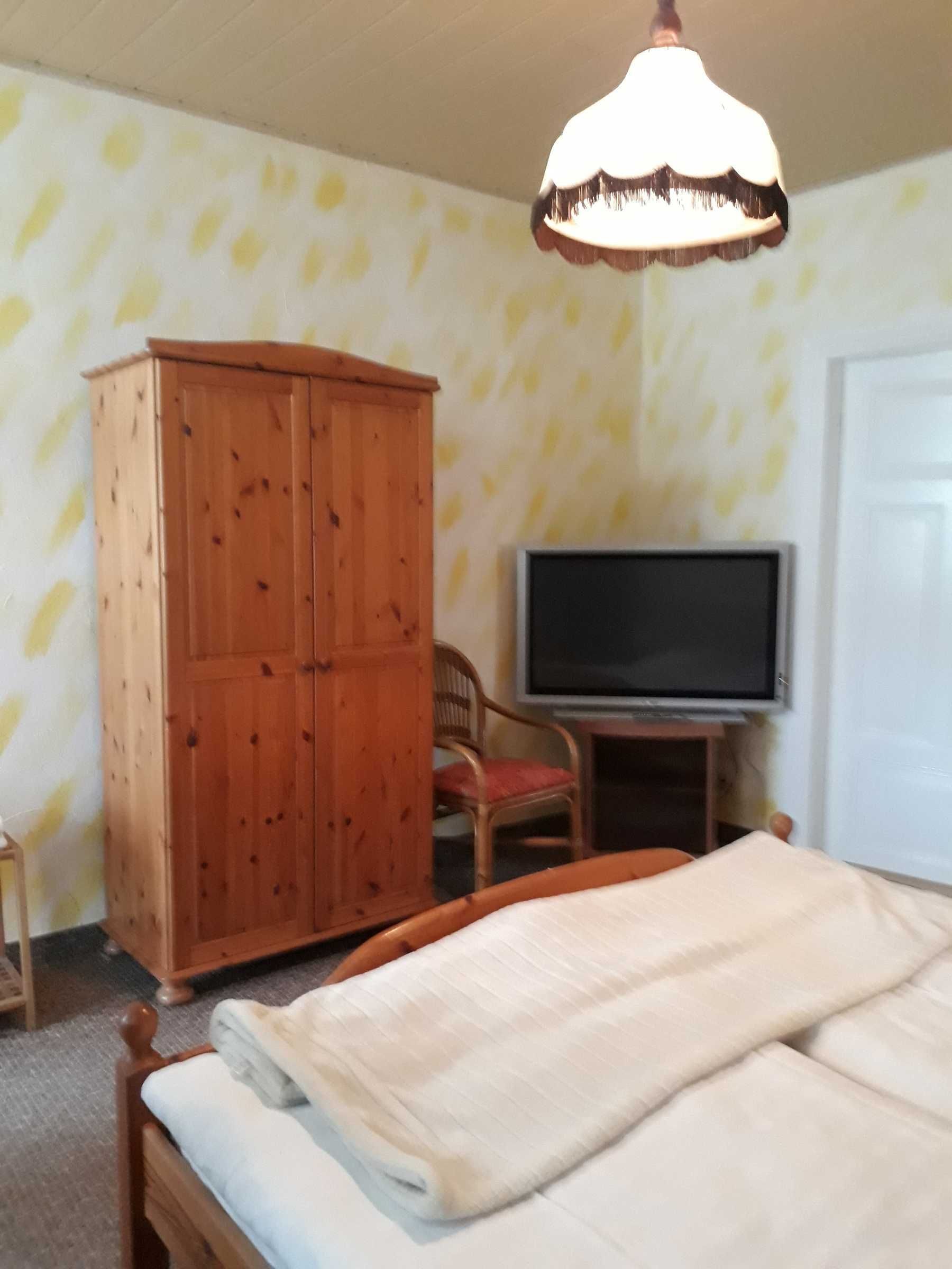 A bedroom with a bed, a wooden wardrobe, a television, and a chair.