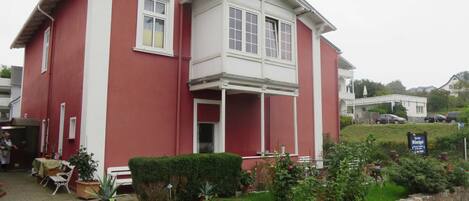A red and white two-story building with a balcony, potted plants, and a stone wall.
