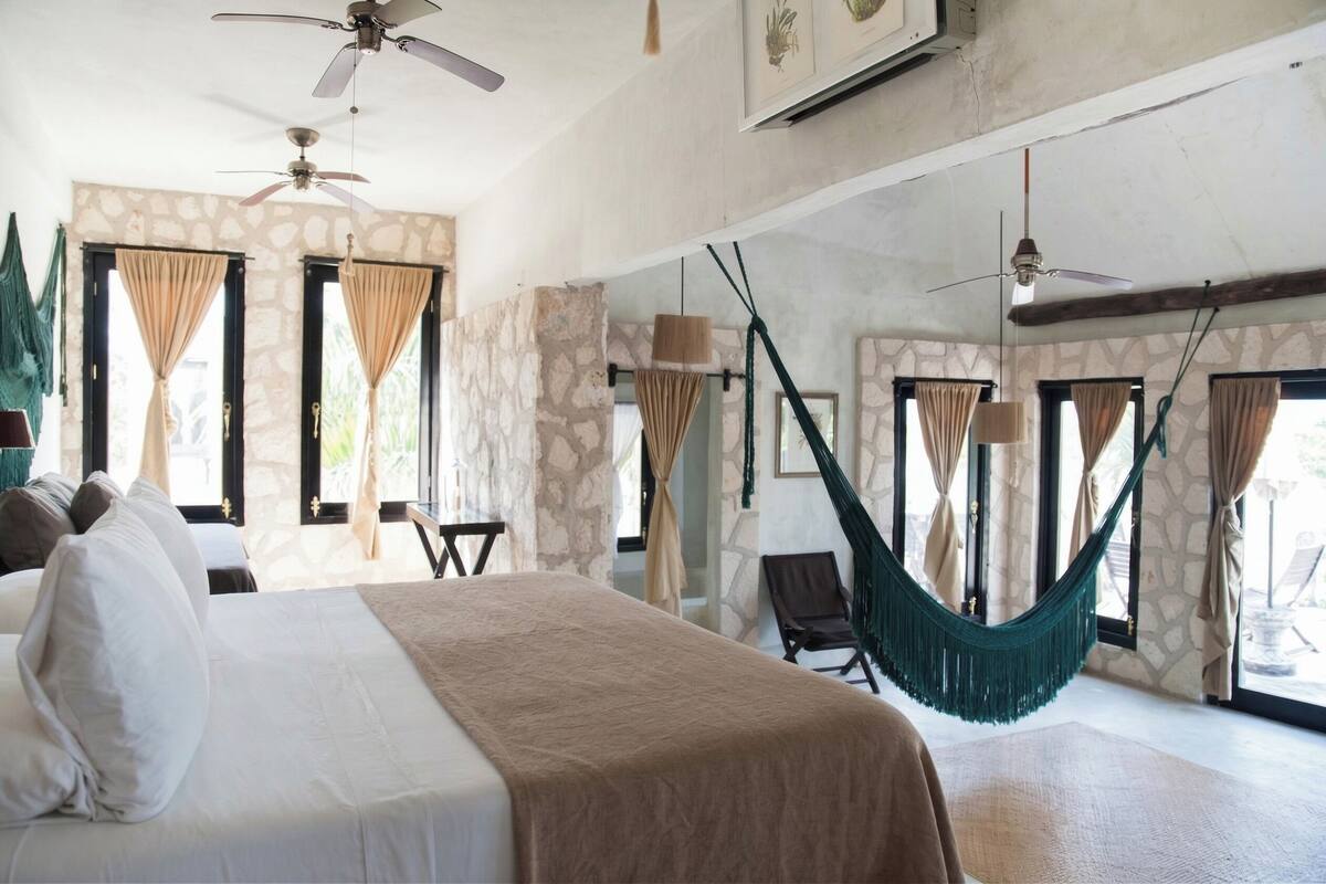 A bedroom with a bed, two ceiling fans, a hammock, and a view of the outdoors.