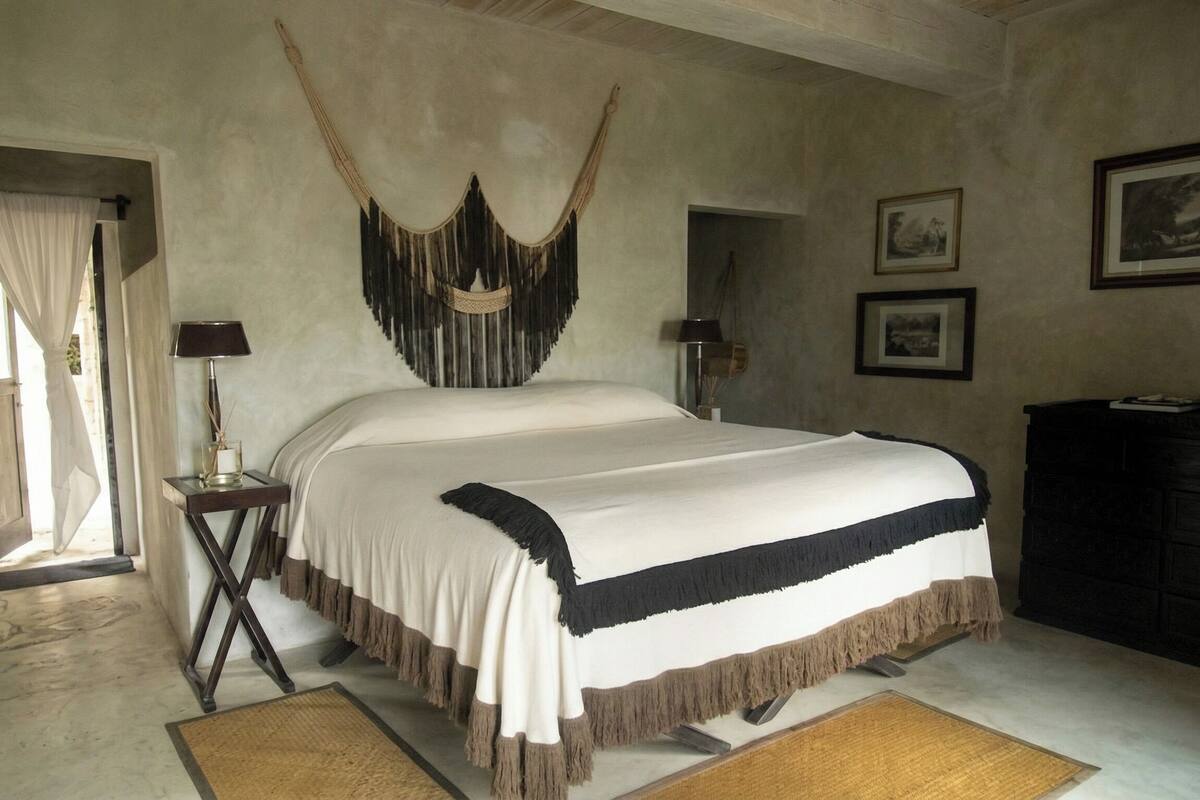 A bedroom with a bed, two bedside tables, a hanging chair, a dresser, and a door.