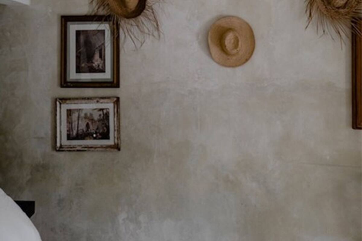 A bedroom with a bed, two framed pictures, and two hats on the wall.