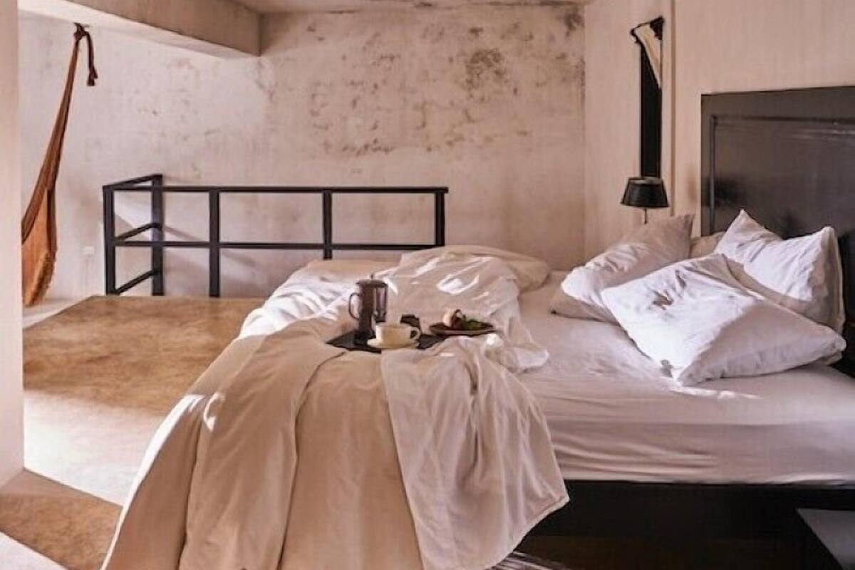 A single bed with a headboard, a bedside table with a lamp, and a hanging brown bag.