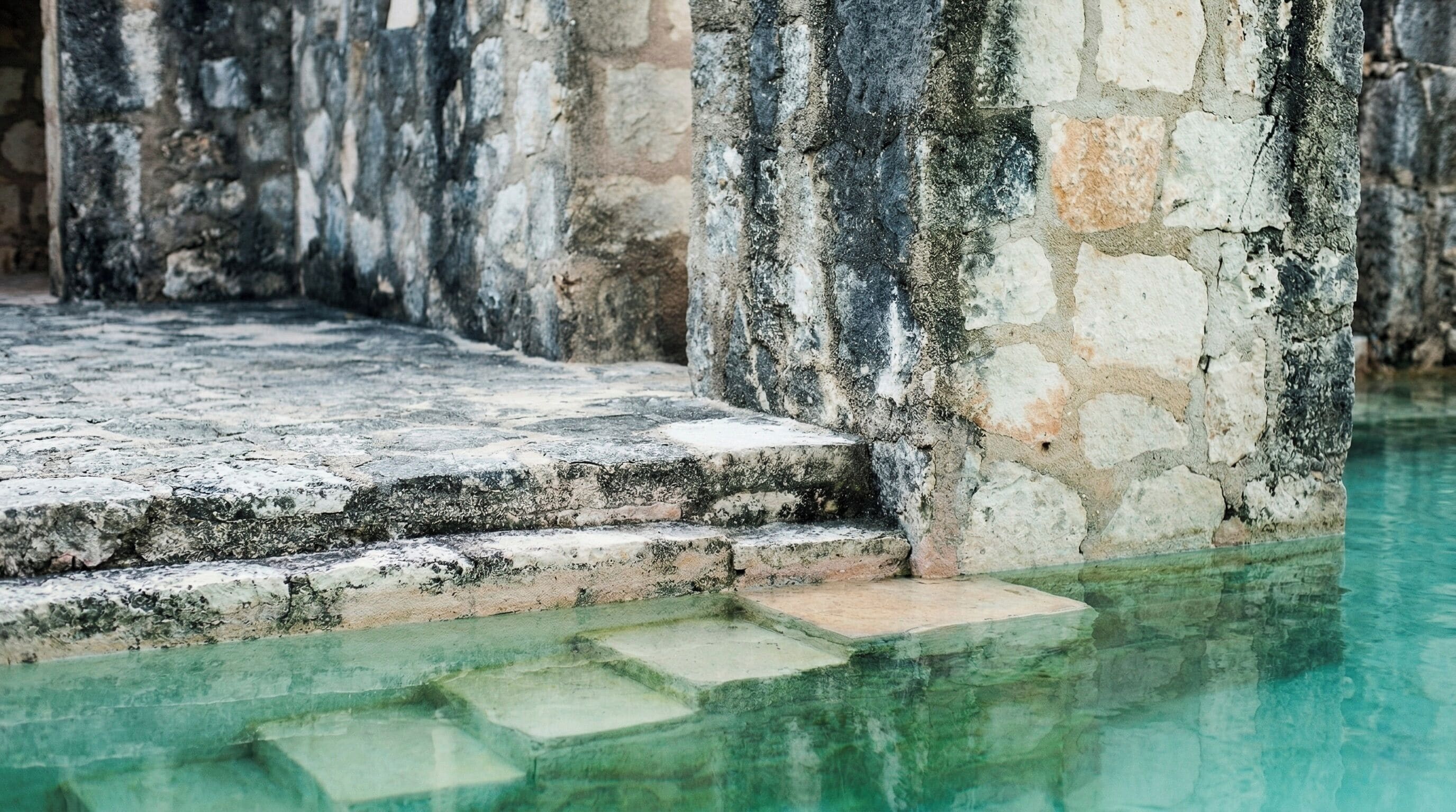 Uma piscina de pedra com degraus que a levam, rodeada por paredes de pedra desgastada.