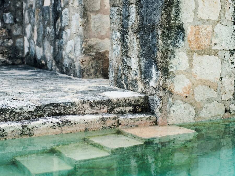 Uma piscina de pedra com degraus que a levam, rodeada por paredes de pedra desgastada.
