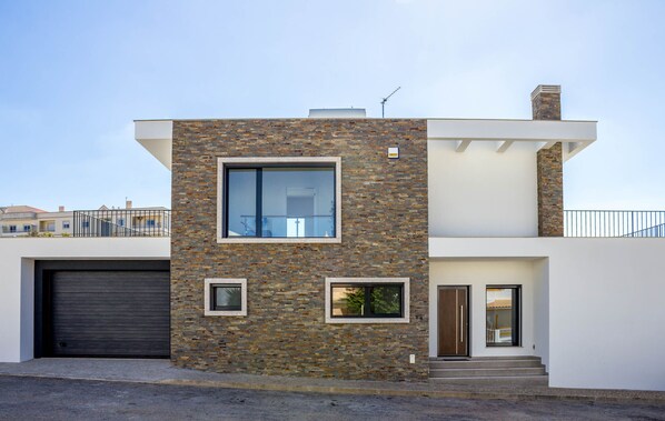 A modern two-story house with a stone facade, a garage, and a balcony.