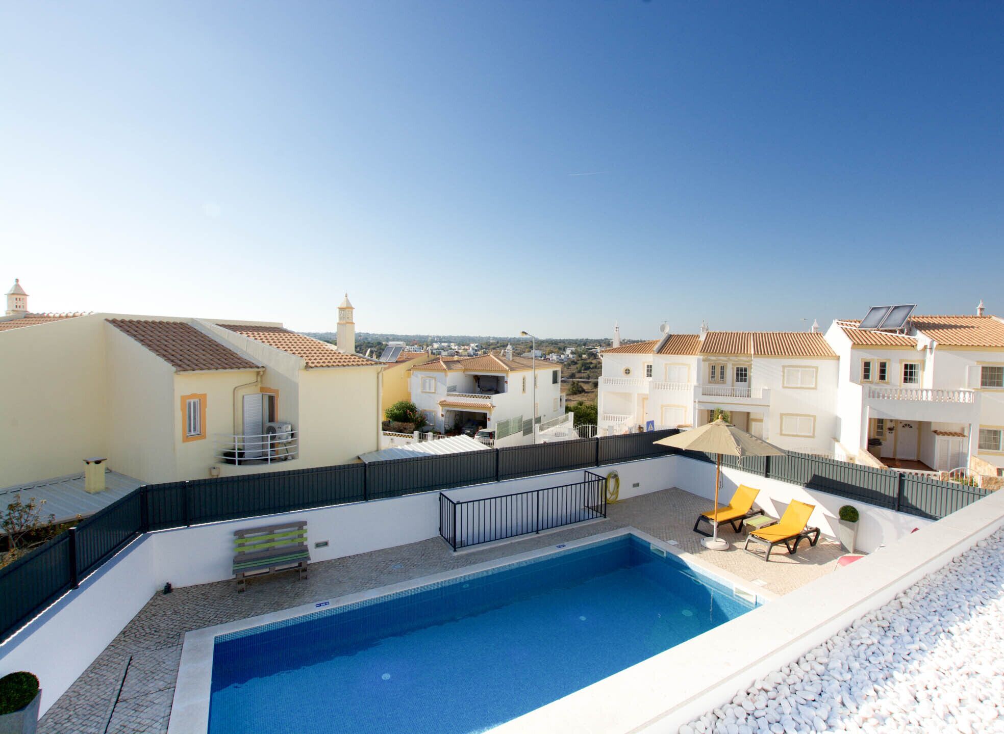 Ein Dachpool mit Blick auf umliegende Häuser, einer Bank und einem gelben Sonnenschirm.