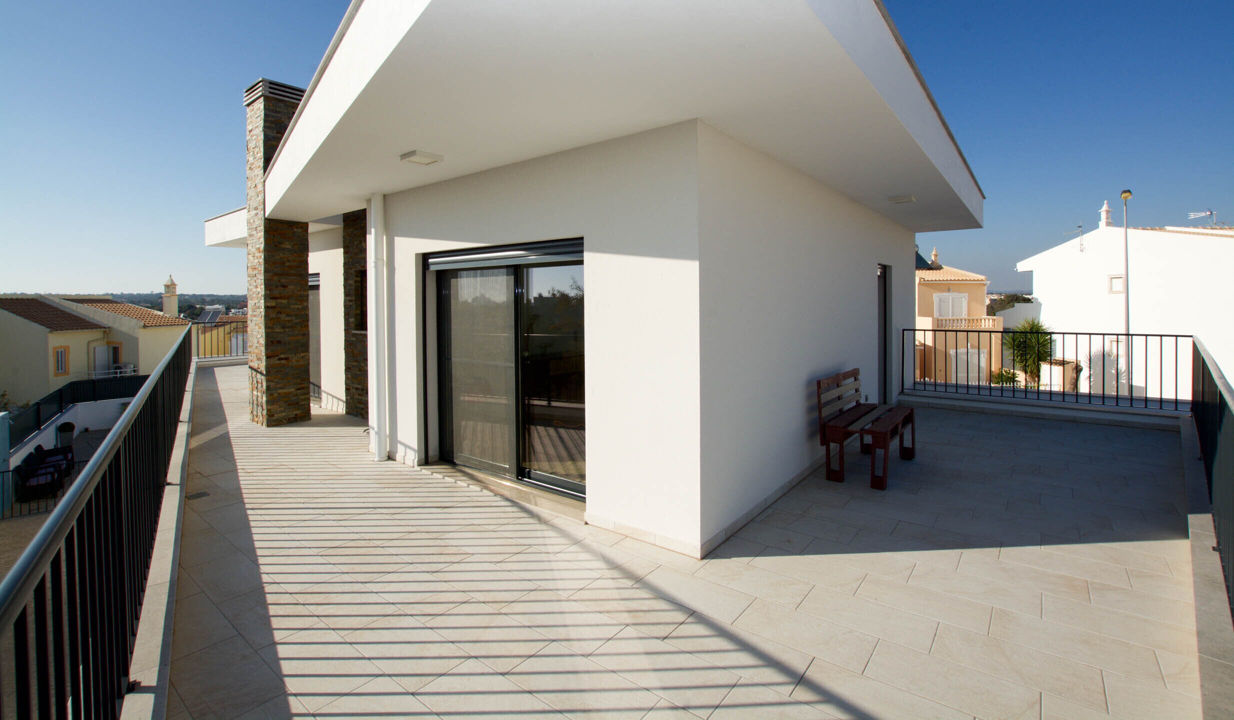 A modern balcony with a glass door, a bench, and a view of the neighborhood.