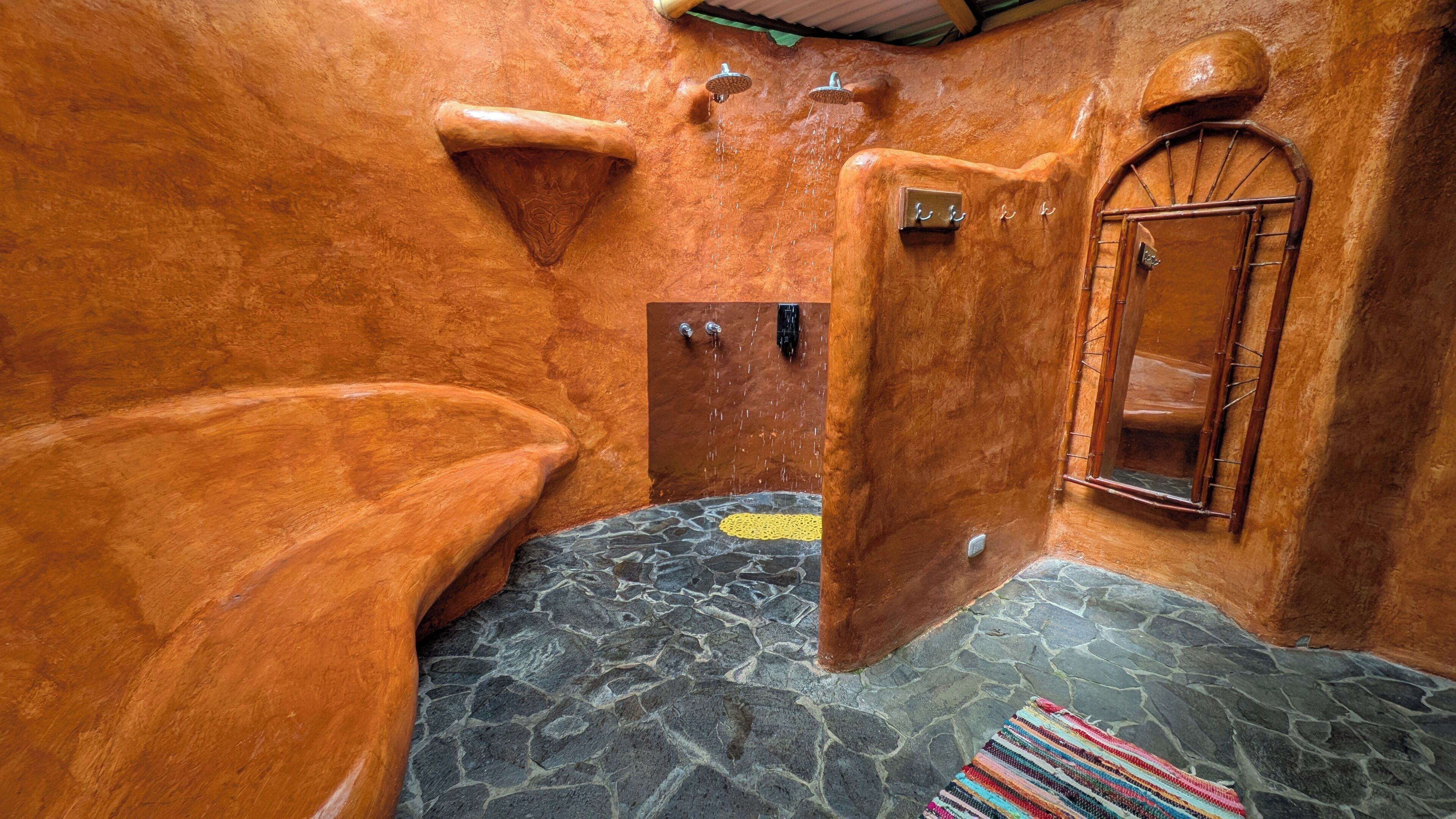 Un baño rústico con suelo de piedra, una bañera de madera, ducha y una ventana pequeña.