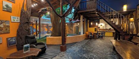 A rustic interior with stone flooring, wooden furniture, and a staircase leading to an upper level.