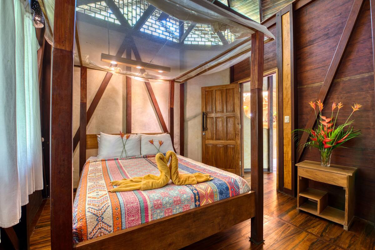 Een hemelbed met een kleurrijke quilt, een houten hoofdbord en een dakraam erboven.