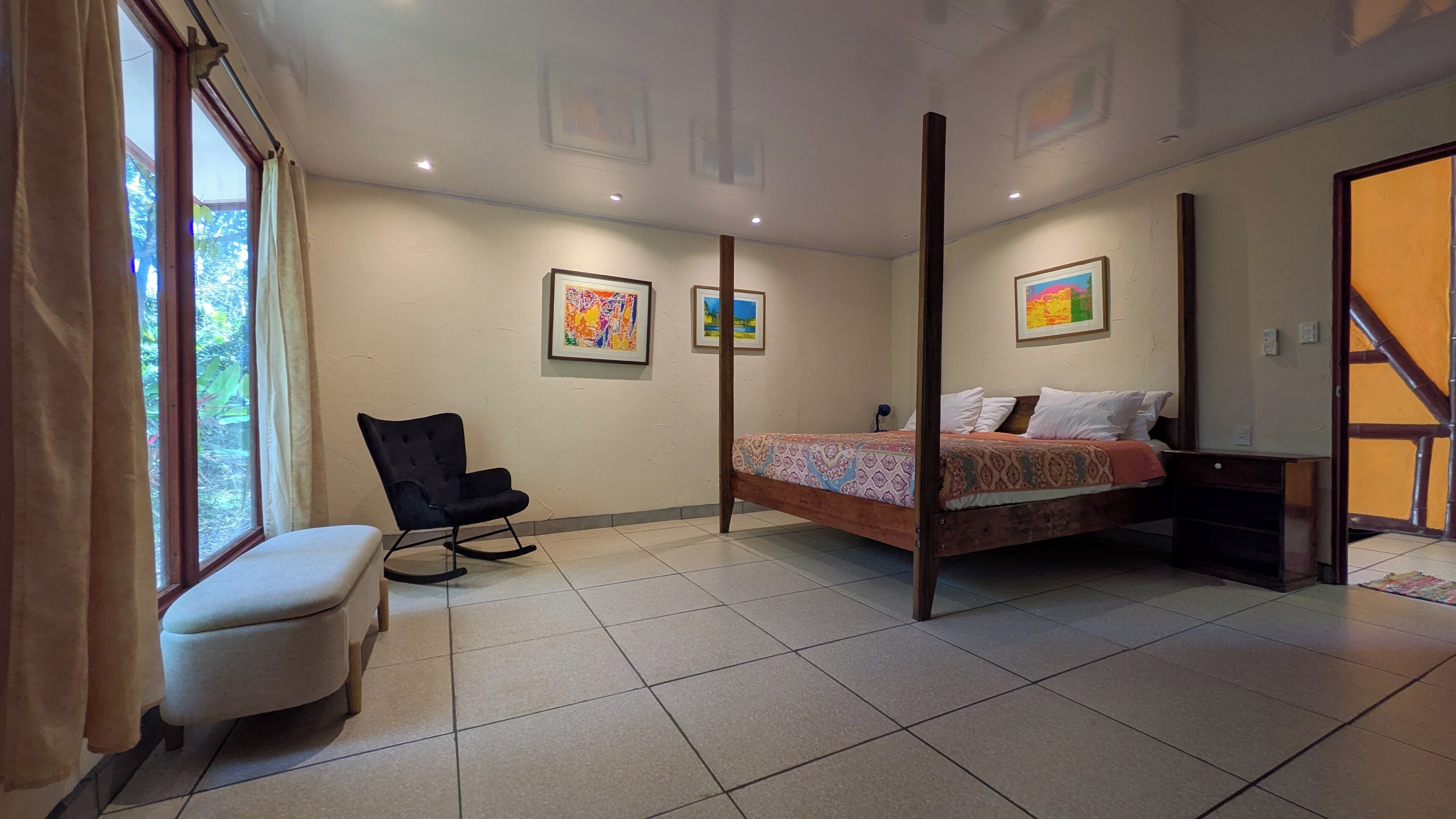 Un dormitorio con cama con dosel, una mecedora, un banco y dos cuadros en la pared.