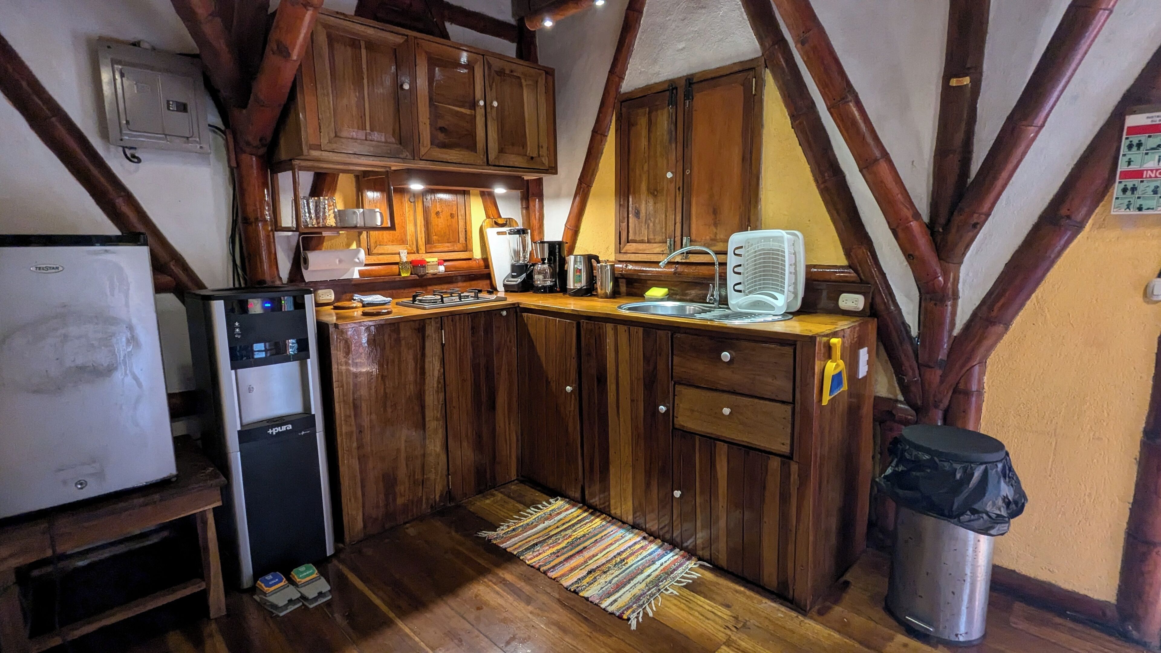 A compact kitchen with wooden cabinets, a refrigerator, a sink, and a trash bin.