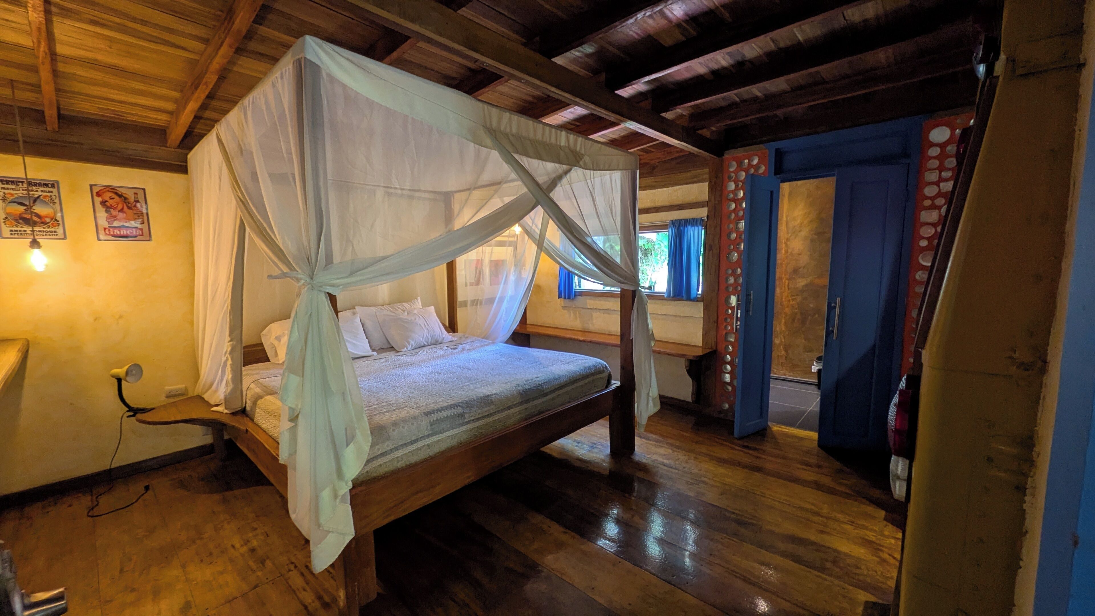 Una cama con dosel de madera y cuatro columnas, una lámpara de noche y un aplique de pared.