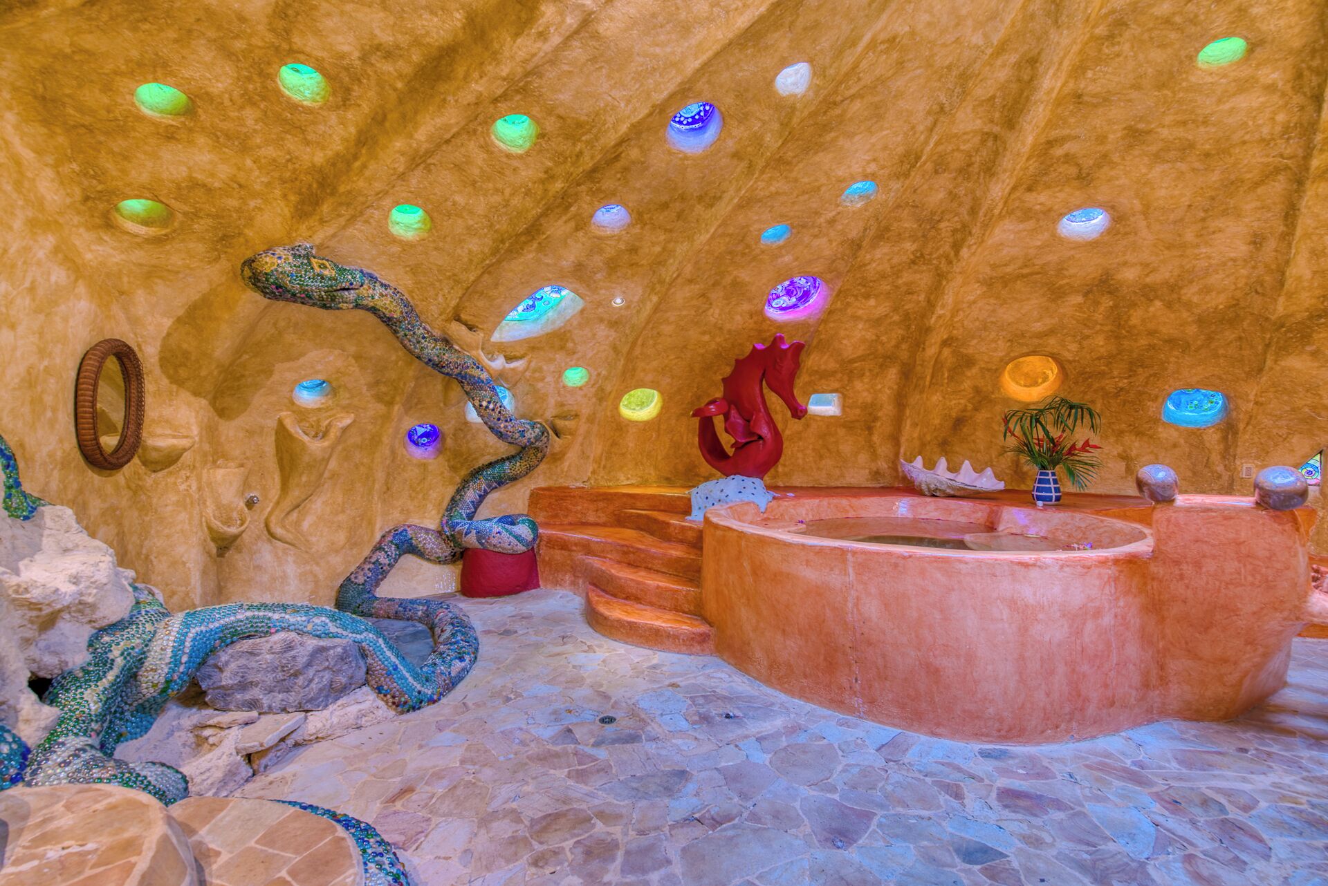 A bathroom with a stone floor, a bathtub, and a decorative wall with a snake and a red horse sculpture.