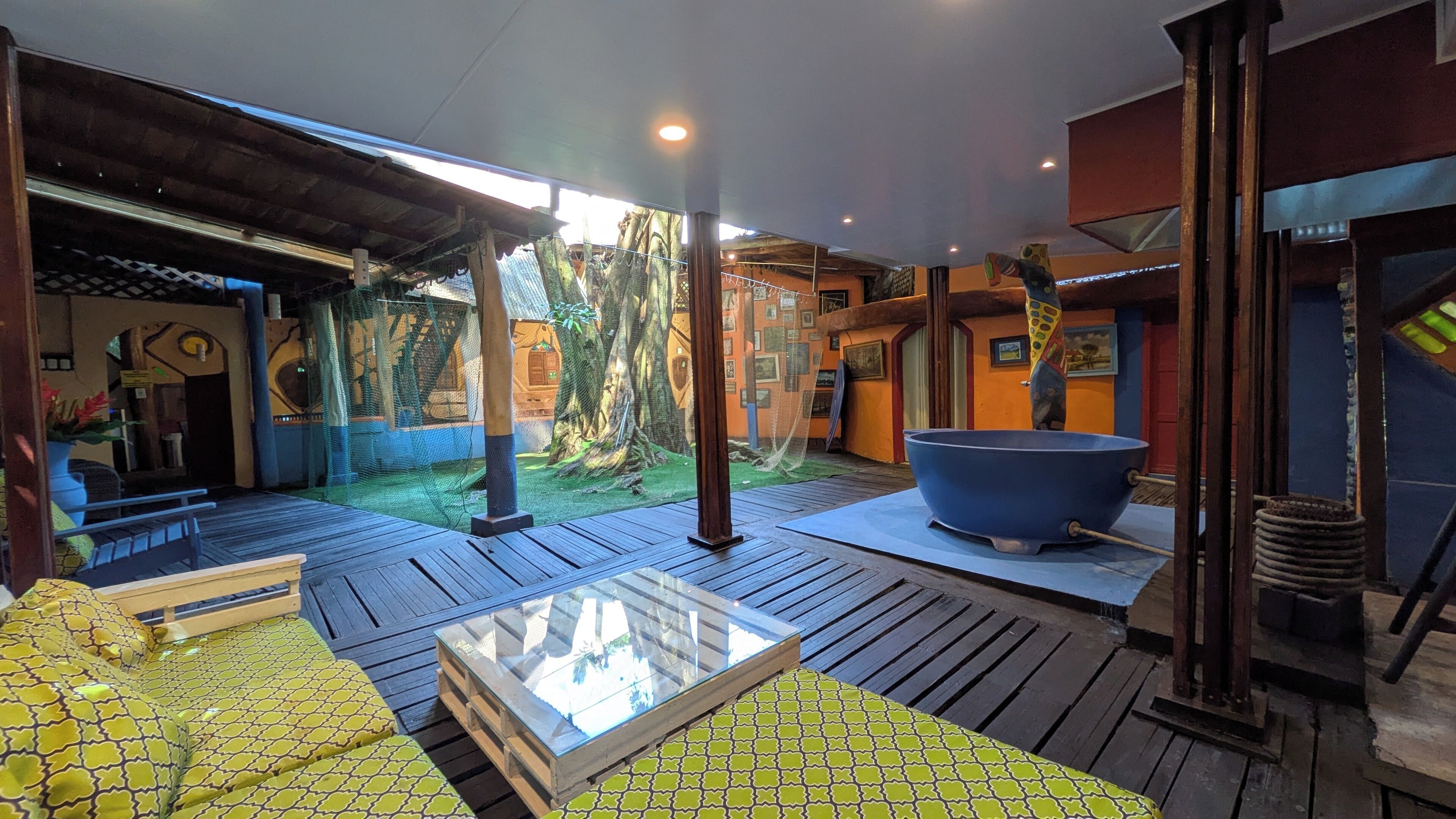 An outdoor patio with wooden flooring, a glass-top table, and a large blue basin.