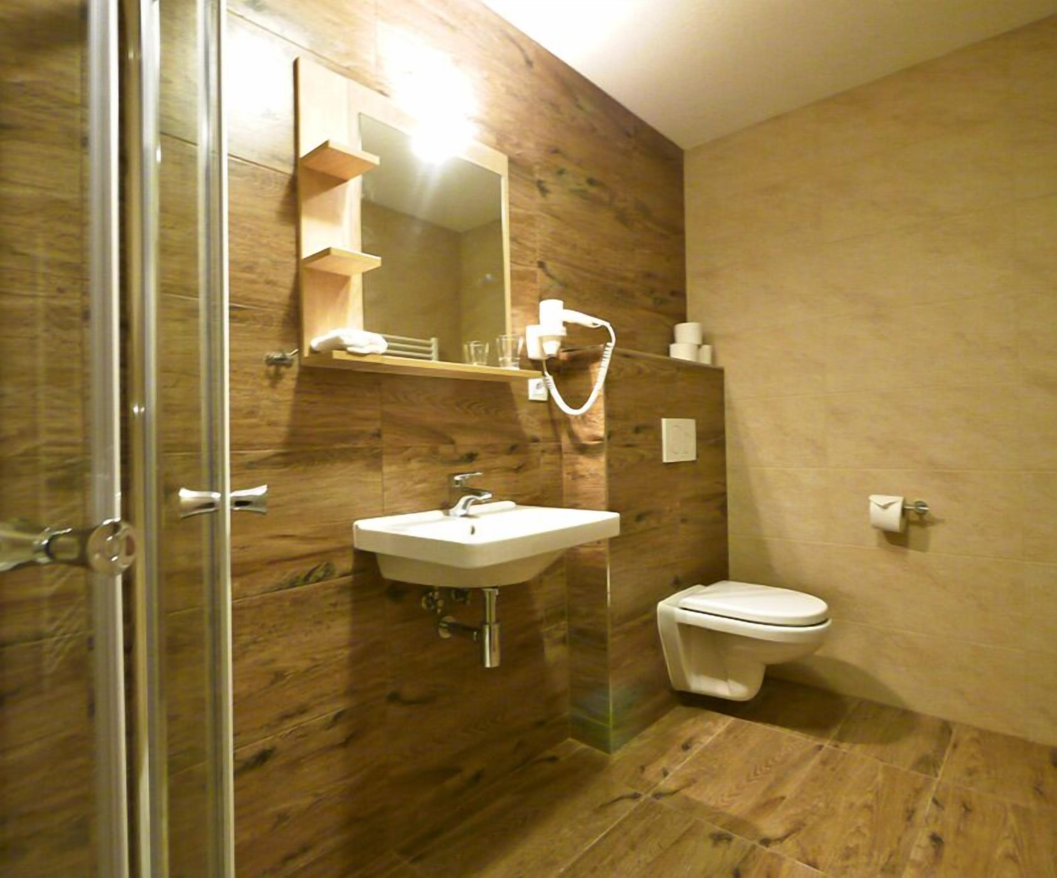 A bathroom with a wooden wall, a sink, a toilet, and a glass shower enclosure.