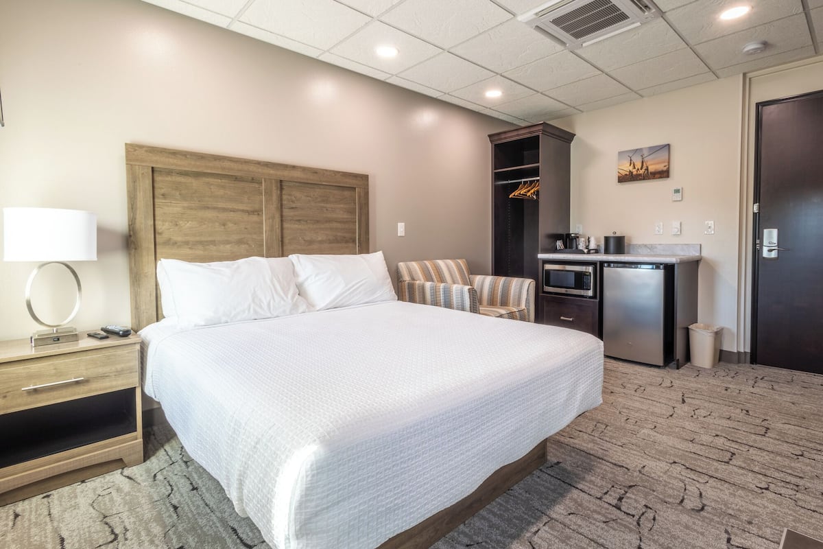 A hotel room with a large bed, a desk with a lamp, a microwave, and a small kitchenette.