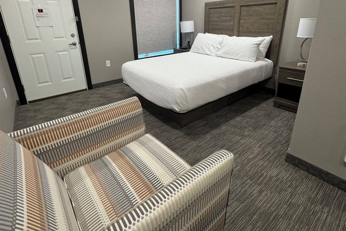 A hotel room with a large bed, a sofa, a desk with a lamp, and a door with a sign.
