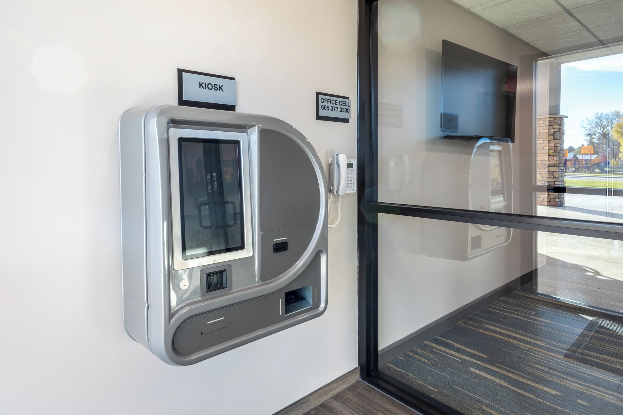 A modern office space with a glass door, a kiosk, and an office phone.