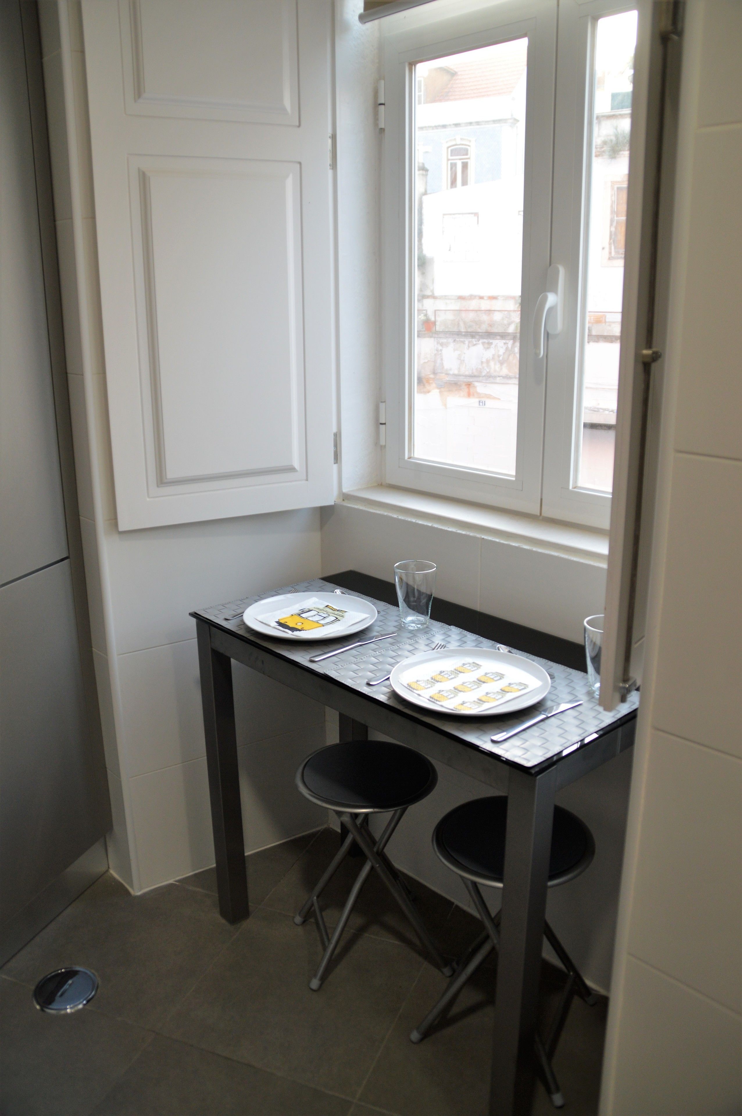 A small kitchen with a window, a table with plates and cutlery, two chairs, and a door.