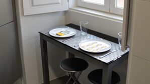 Una cuina petita amb una finestra, una taula amb plats i coberts, dues cadires i una porta.