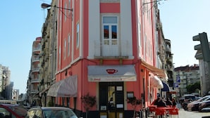 Un edifici als angles amb un restaurant a la planta baixa, façana vermella i blanca, seients a l'exterior i vista del carrer.
