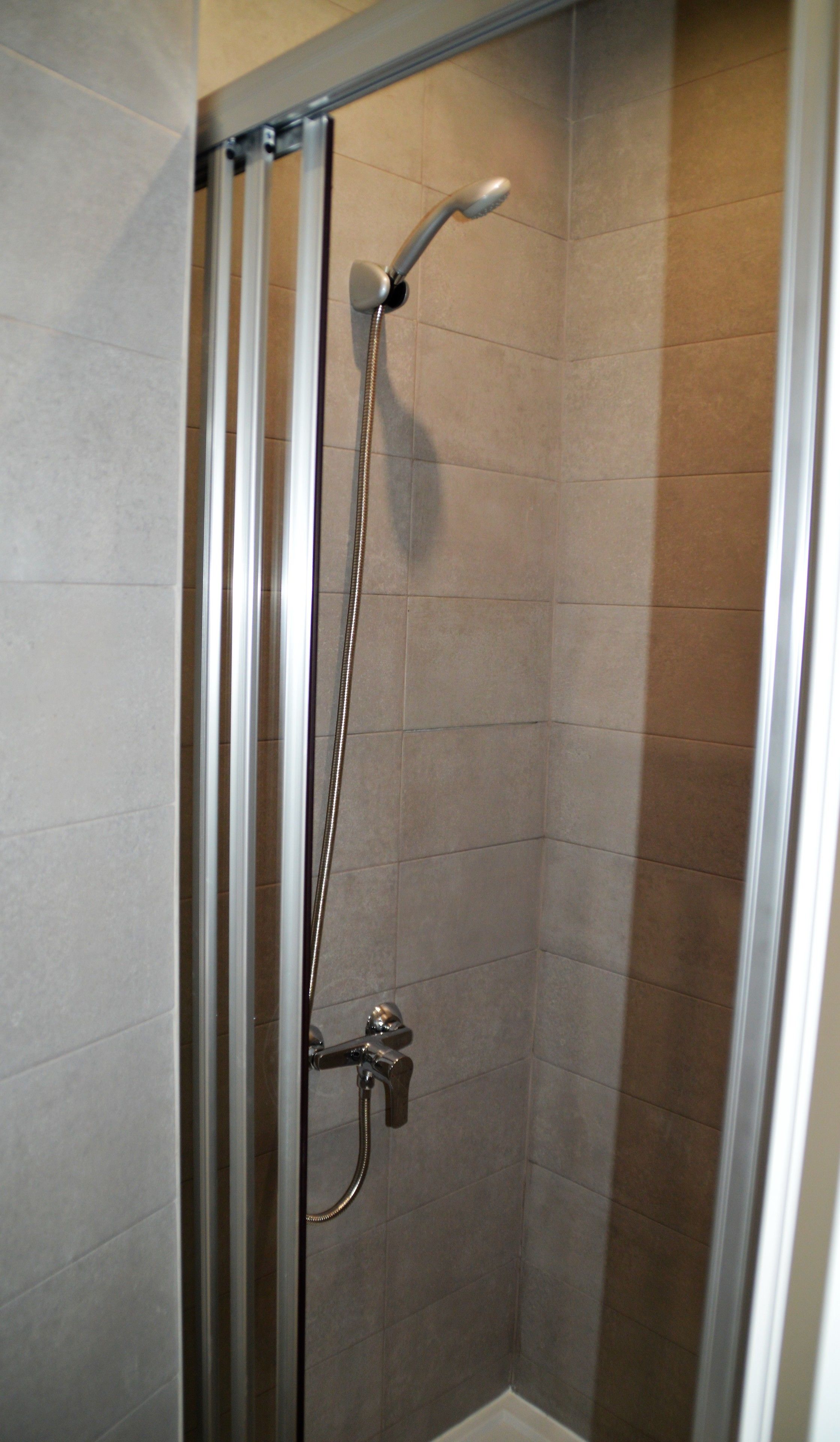 A shower with a handheld showerhead and a wall-mounted faucet.