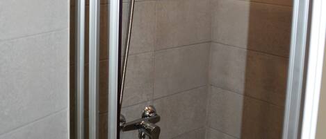 A shower with a handheld showerhead and a wall-mounted faucet.
