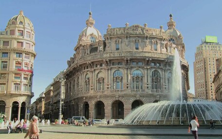 A historic building with ornate architecture, a central fountain, and surrounding modern buildings.