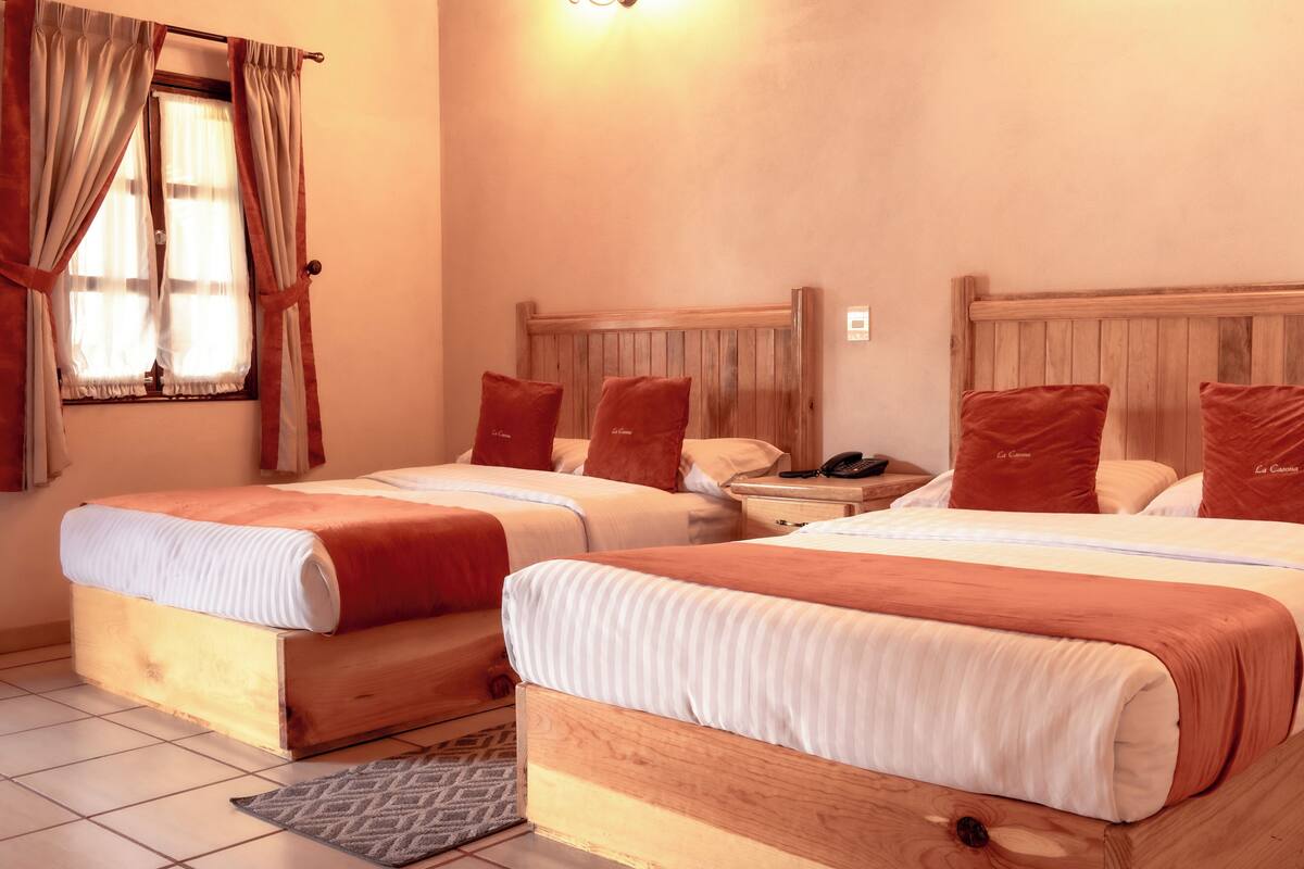 Une chambre d’hôtel avec deux lits en bois, des murs de couleur beige et une fenêtre avec des rideaux.