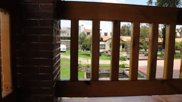 Un balcón de madera con un muro de ladrillo y vistas a un área residencial con casas y vegetación.