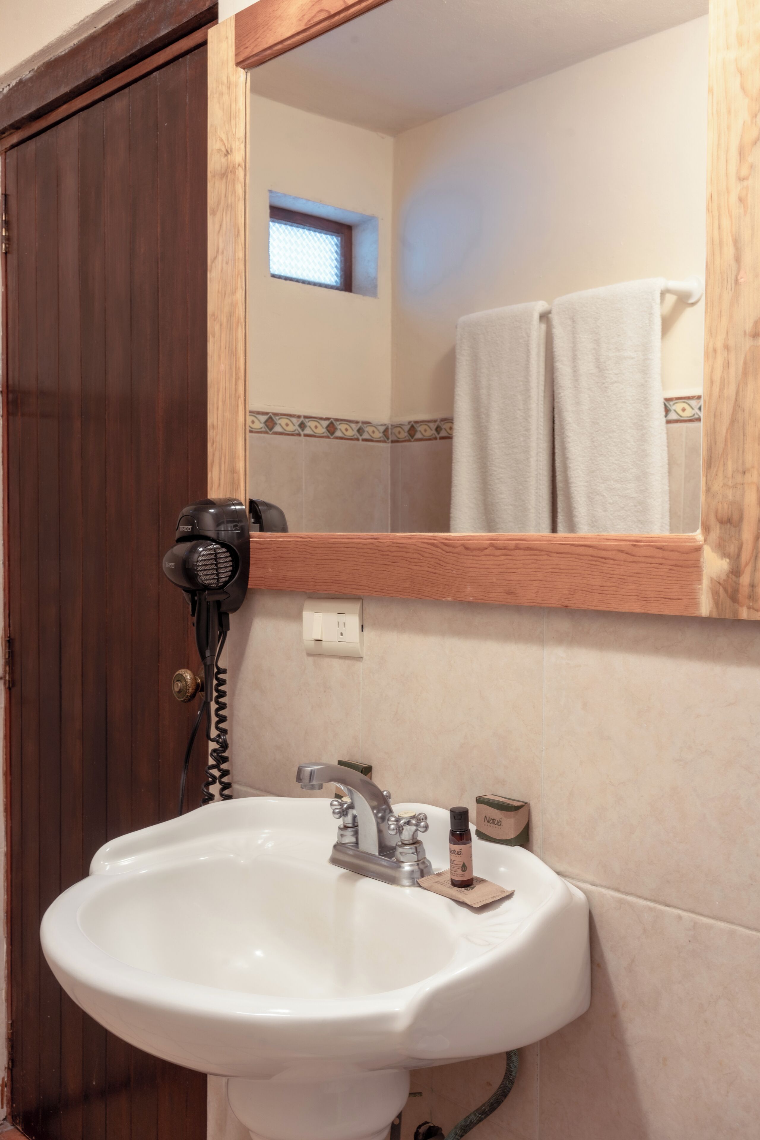 Un baño con un lavamanos blanco, un secador de pelo y un espejo encima.