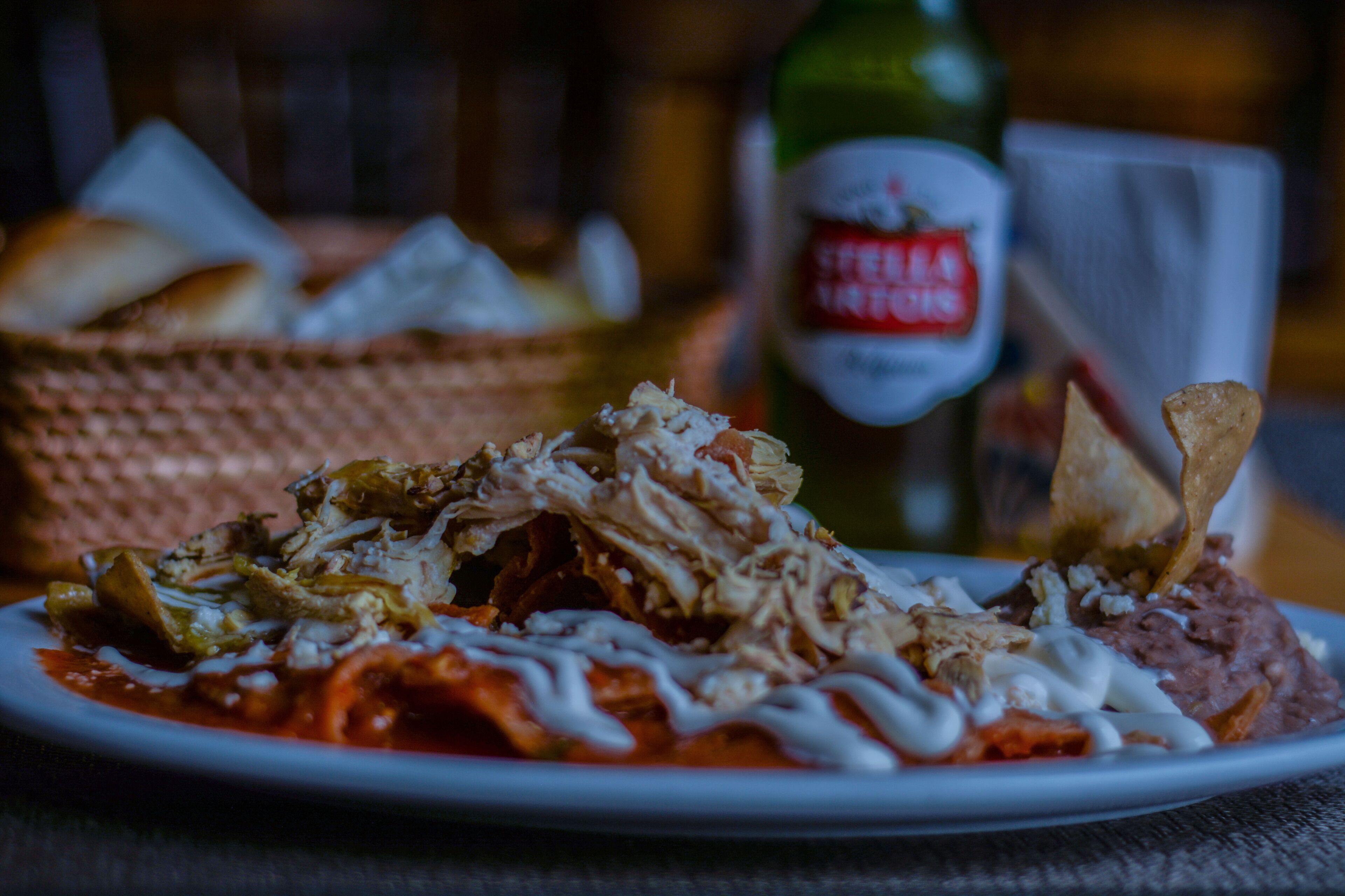A plate of food with shredded meat, beans, and a sauce, accompanied by a bottle of beer and bread.