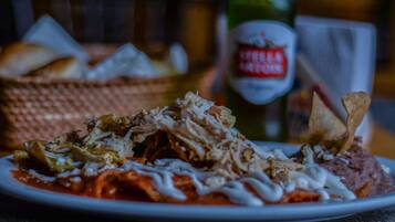 A plate of food with shredded meat, beans, and a sauce, accompanied by a bottle of beer and bread.