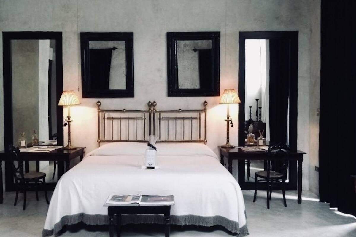 A hotel room with a large bed, two bedside tables with lamps, and three mirrors on the walls.