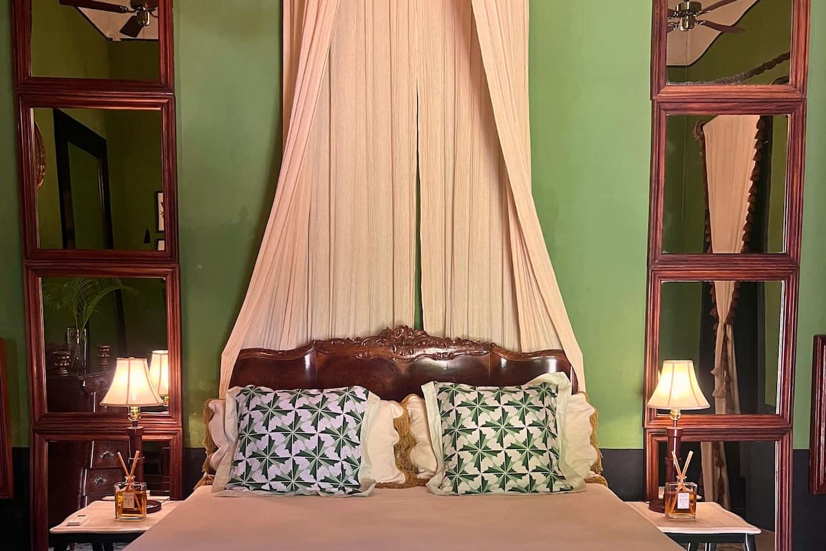 A bedroom with a canopy bed, two nightstands with lamps, and a table with decorative items.