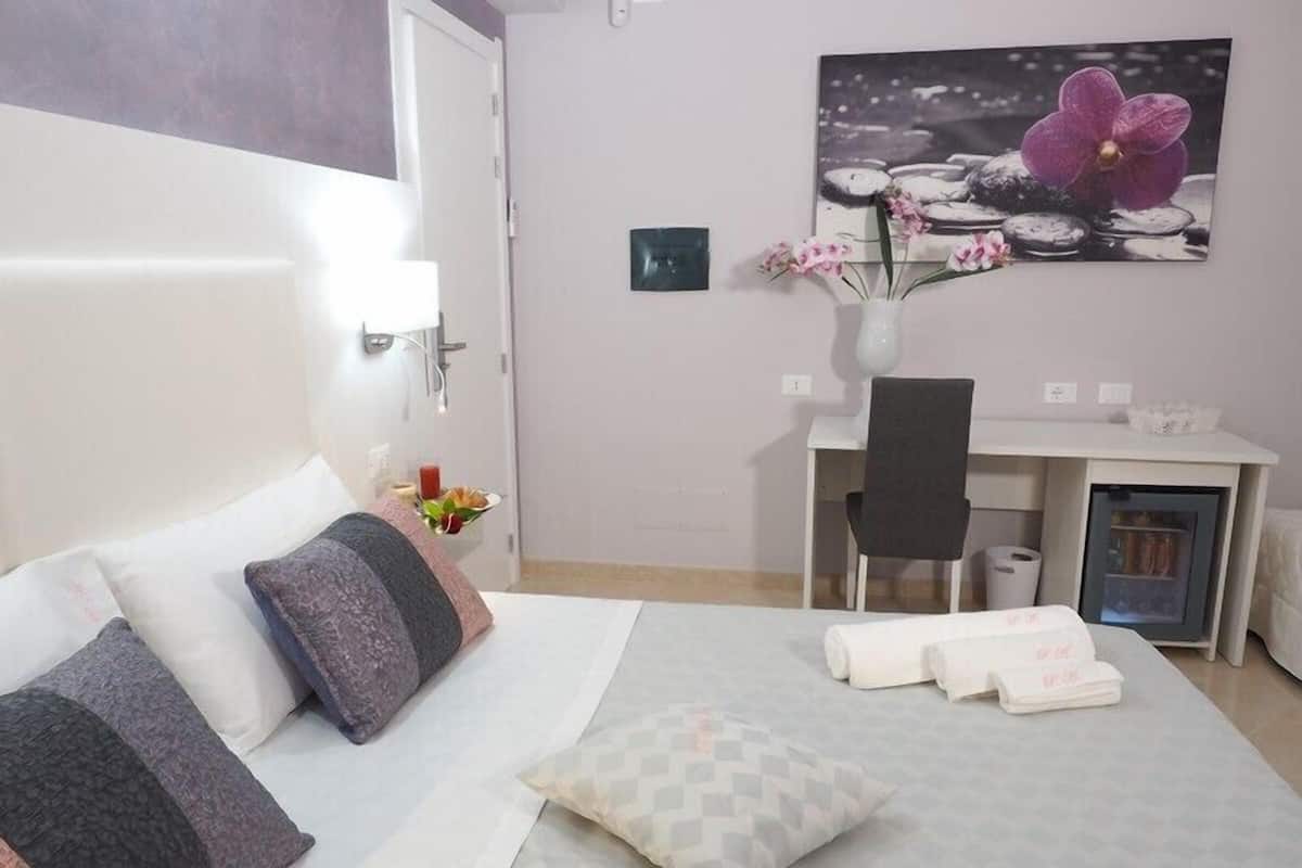 A hotel room with a bed, a desk, a chair, and a small refrigerator.