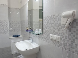 A bathroom with a white sink, a mirror, and a hairdryer on the wall. - Pepè Accommodation (Parghelia)