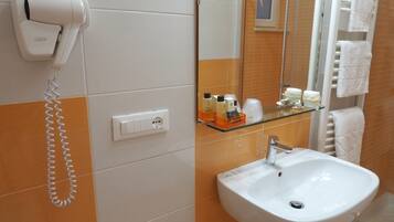 A bathroom with a white sink, a hairdryer, a mirror, and a glass shelf with toiletries.