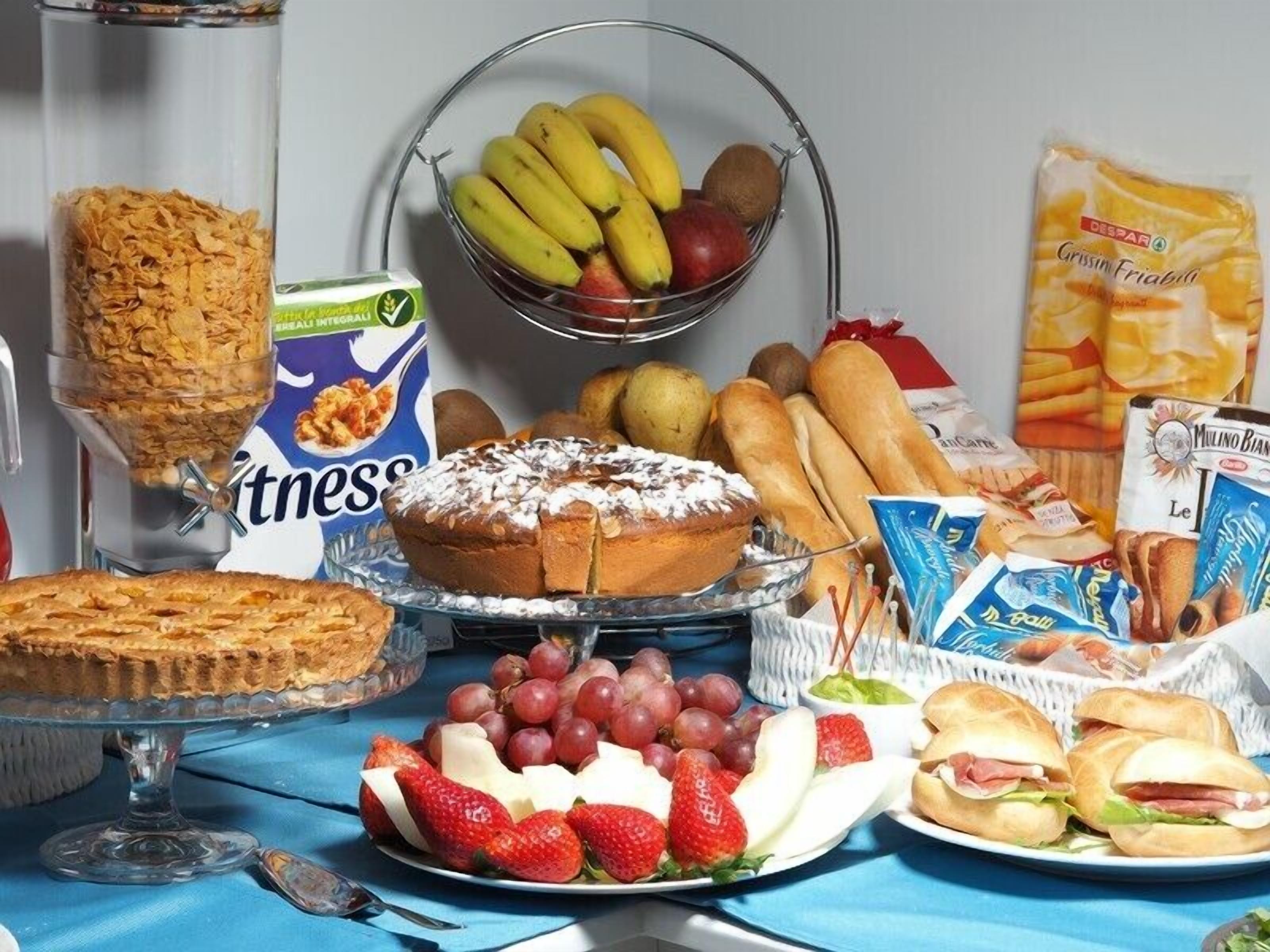 Una mesa de buffet con diversos alimentos, como pastel, fruta, pan y snacks empaquetados.