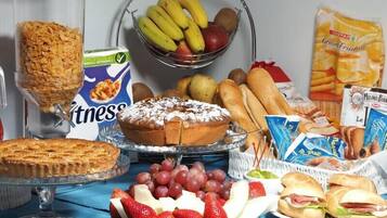 Una mesa de buffet con diversos alimentos, como pastel, fruta, pan y snacks empaquetados.